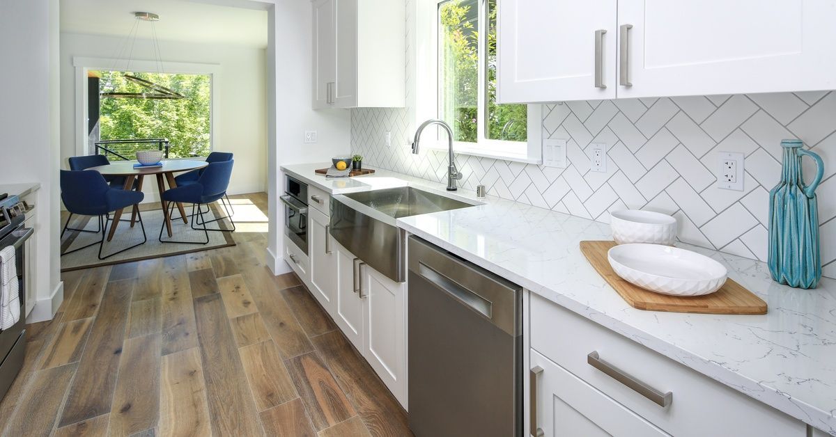 A kitchen in a home that has wooden floors and white cabinets. The countertops are white and made of marble.