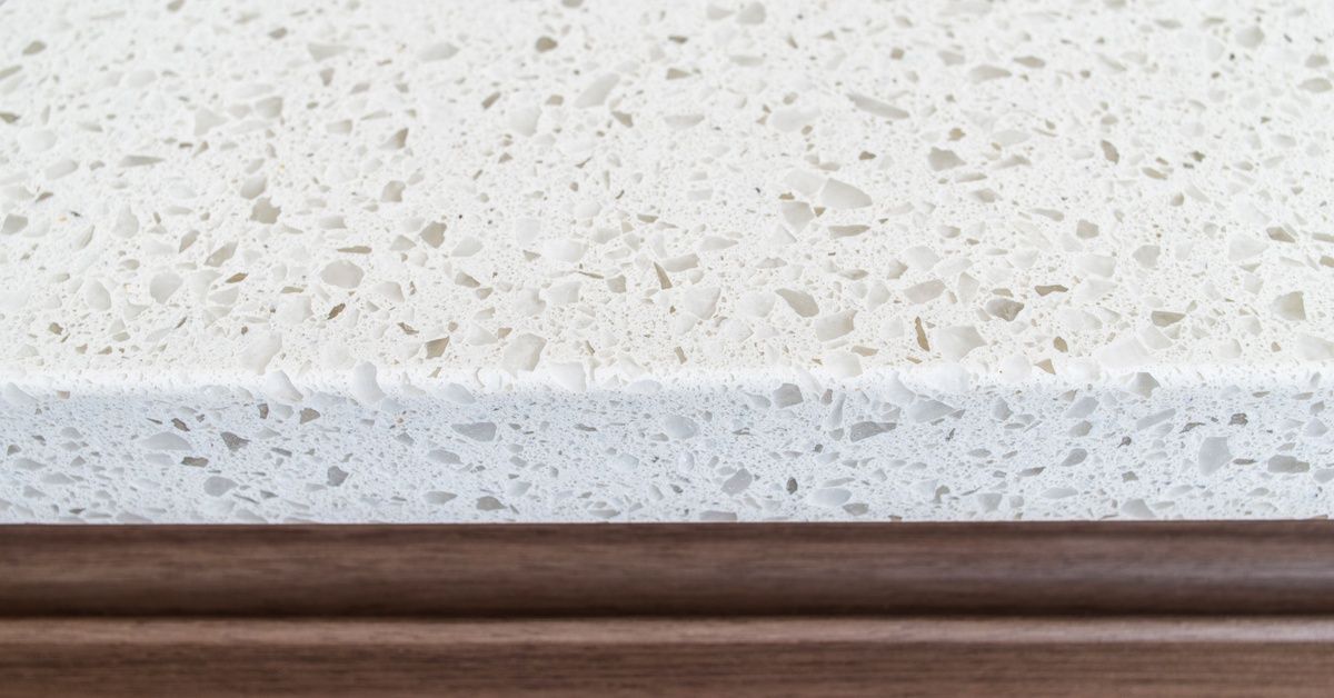 A white countertop made of quartz. The quartz counter is installed on top of a dark brown wooden surface.