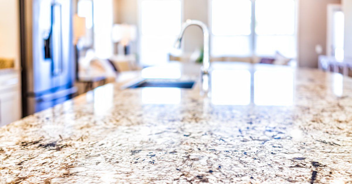 Bright sunlight is shining in from a window. The light reflects on a granite countertop in a residential kitchen.