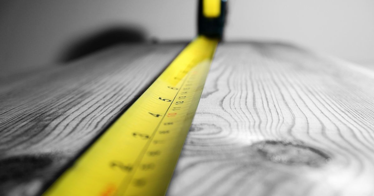 A black-and-yellow tape measure is being pulled across a wooden surface that appears worn and weathered.