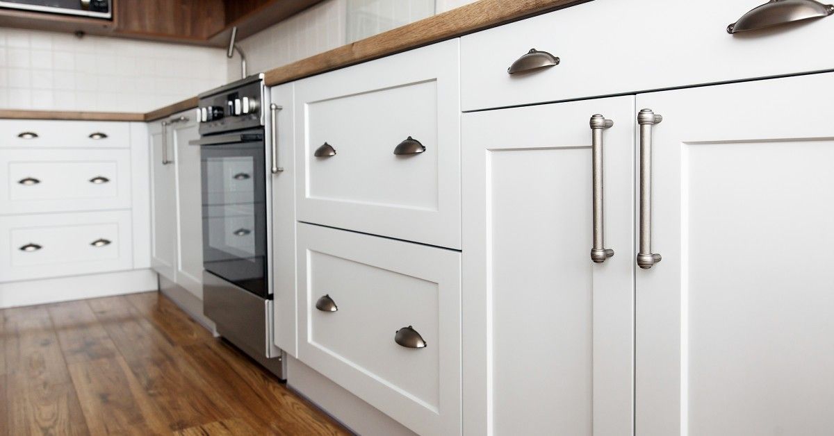 White cabinets in a kitchen that has wooden floors and countertops. The cabinets have silver handles attached to them.