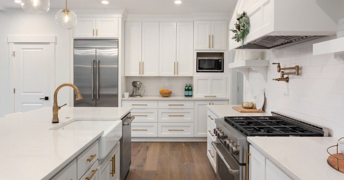 A well-organized residential kitchen with hardwood floors. All the cabinets are white with gold h