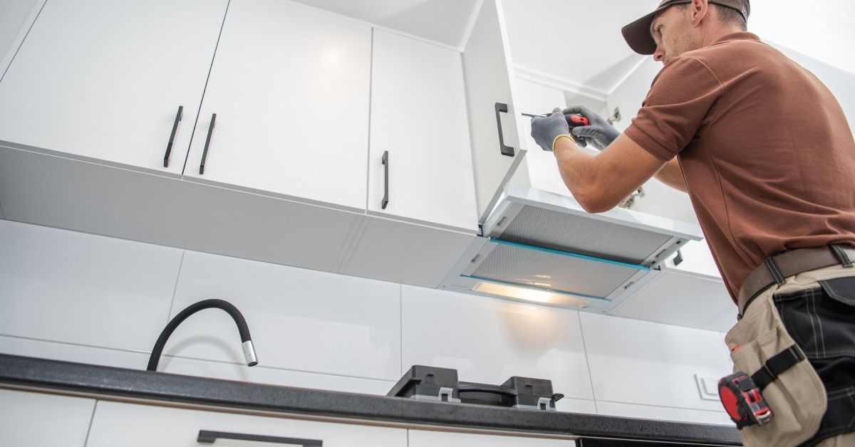 A contractor is installing white cabinets in a residential kitchen. The contractor has a toolbelt around their waist.
