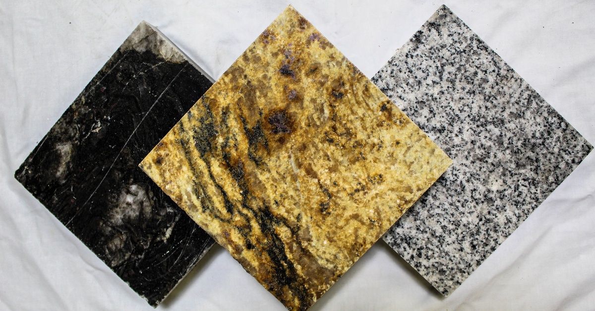 Three small, square granite samples in different colors are lying on top of a white marble surface.