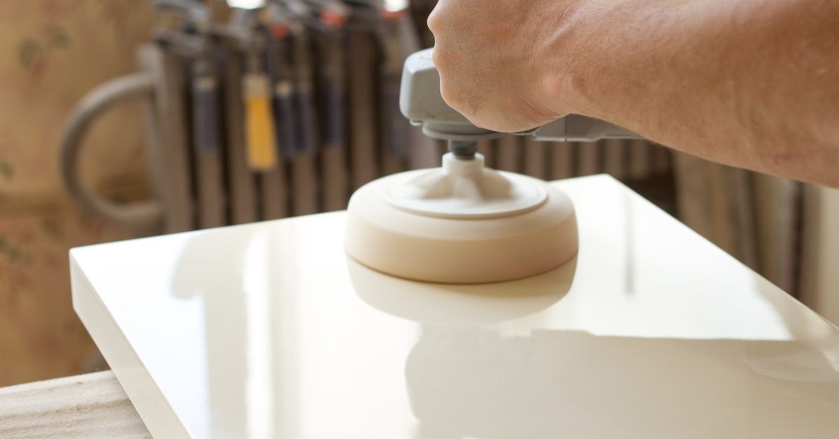 A professional carpenter is using a handheld tool to polish the surface of a shiny white stone countertop.