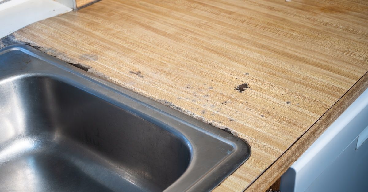 A metal sink installed on a wooden countertop. The counter has black stains and scratches on its surface.