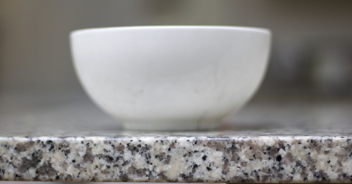 A small white bowl sitting on a granite countertop. The bowl is close to the edge of the counter.
