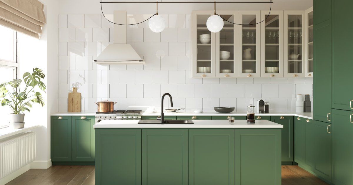 Sunlight streaming into a kitchen with forest green cabinets. The wall is made of large white tiles.