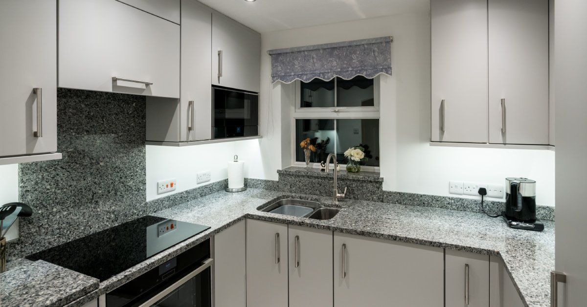 A small residential kitchen with a small window and a granite countertop installed against the wall.