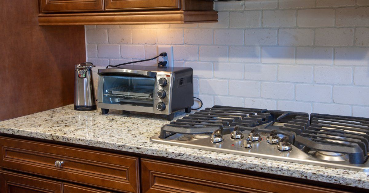 A residential kitchen with a granite countertop and dark wooden drawers. A metal stove is also attached to the counter.