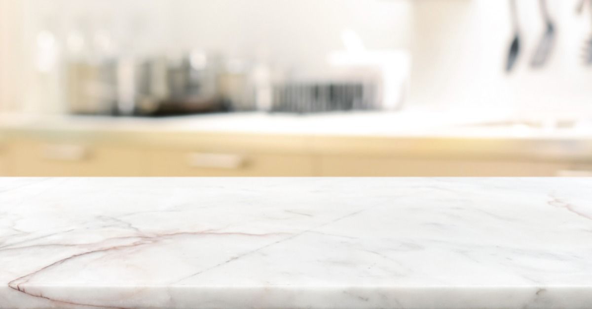 A huge white marble countertop with nothing on top of it. The countertop is in a brightly lit residential kitchen.