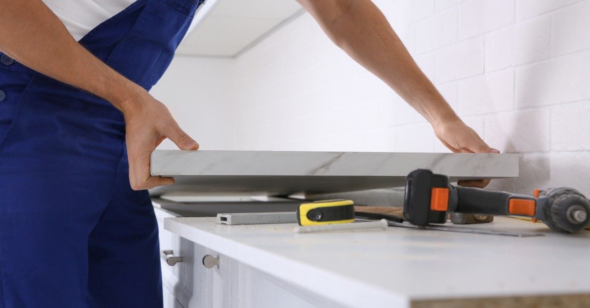 A professional countertop installer holding a stone slab and wearing blue overalls.