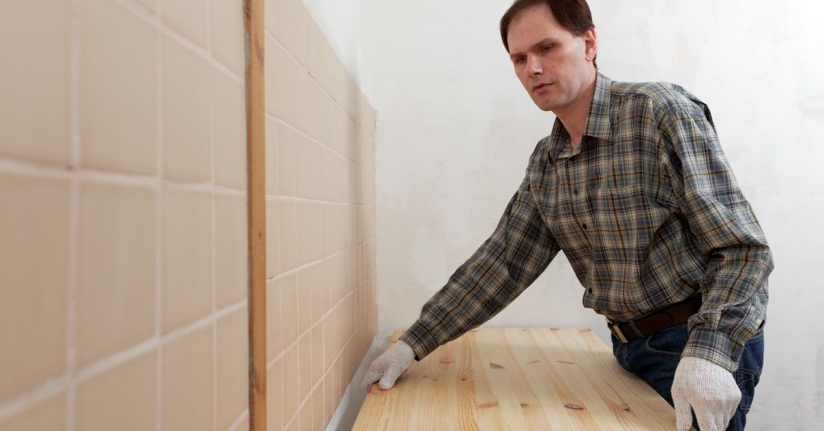 A person wearing white gloves installing a large wooden countertop against a wall inside a building.