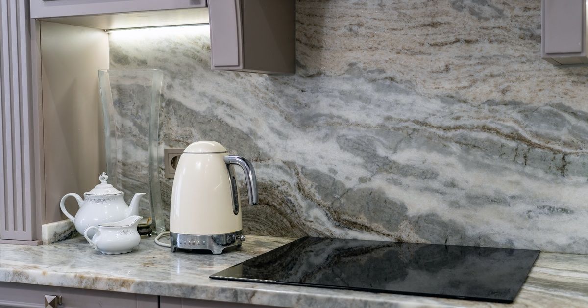 A kitchen countertop with a stovetop on it. A coffee pot and two smaller kettles are next to the stovetop.