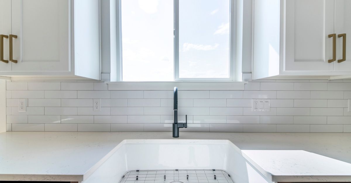 A white sink in the center of a kitchen countertop. The sink is positioned directly in front of a small window.