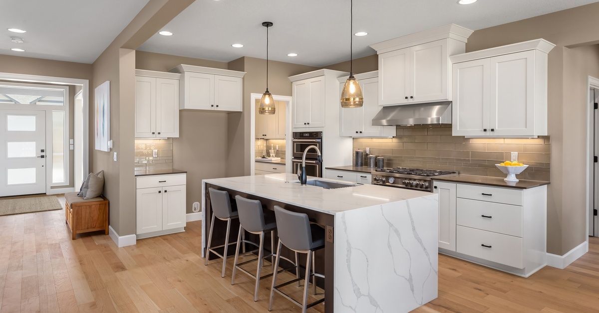 A large, brightly lit residential kitchen with wooden floors and a quartz countertop cut with a waterfall edge.