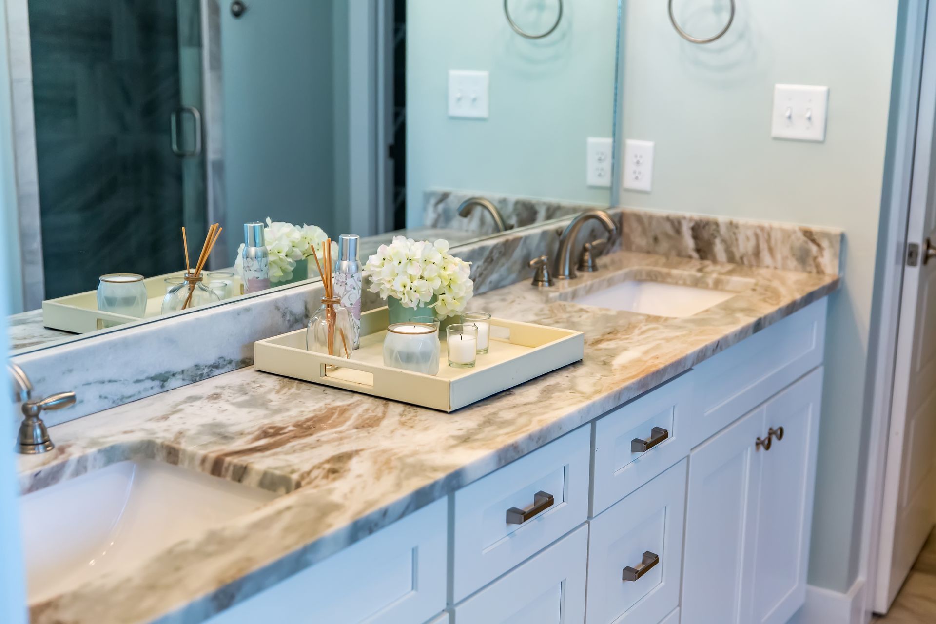 A residential bathroom with a granite countertop. Two sinks are installed in the counter next to a small flower pot.