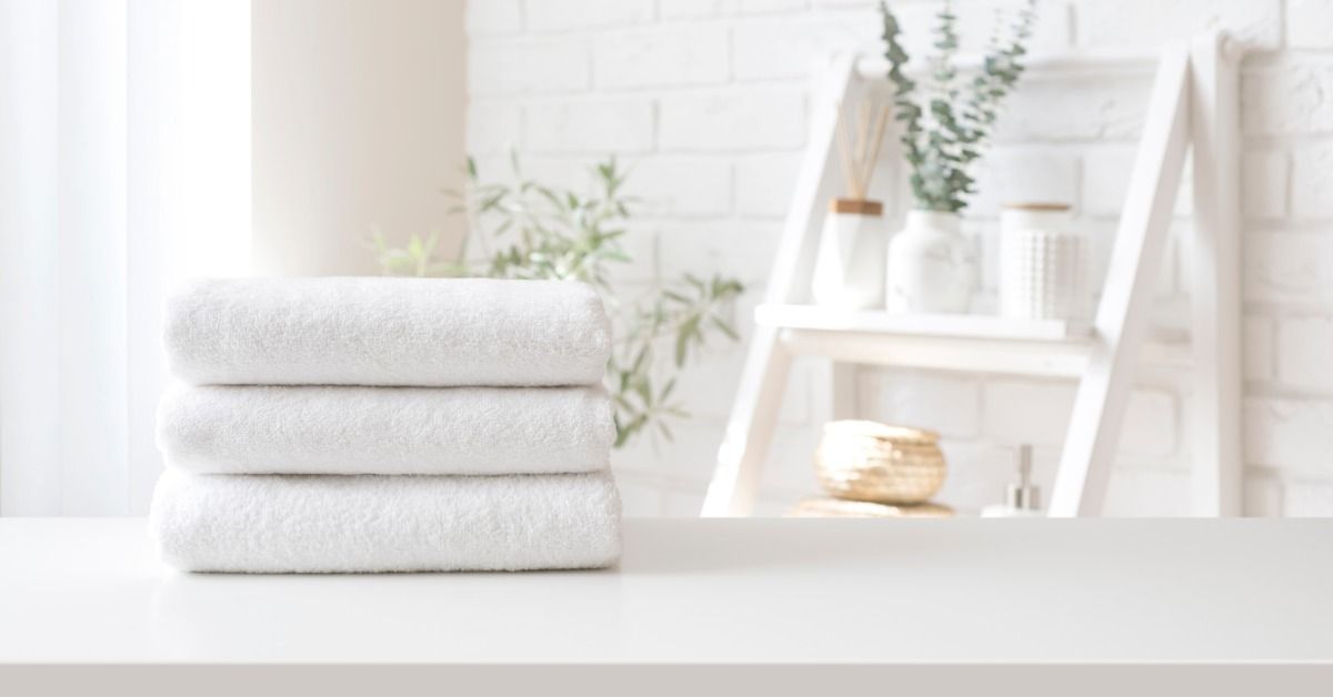 Three clean white towels neatly folded and stacked on top of a white stone counter in a residential bathroom.