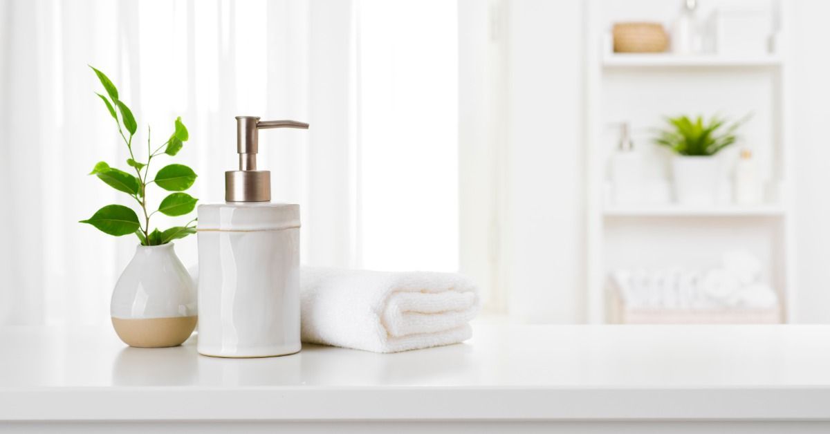 A potted plant, soap dispenser, and folded hand towel are all on a white stone vanity in a large bathroom.