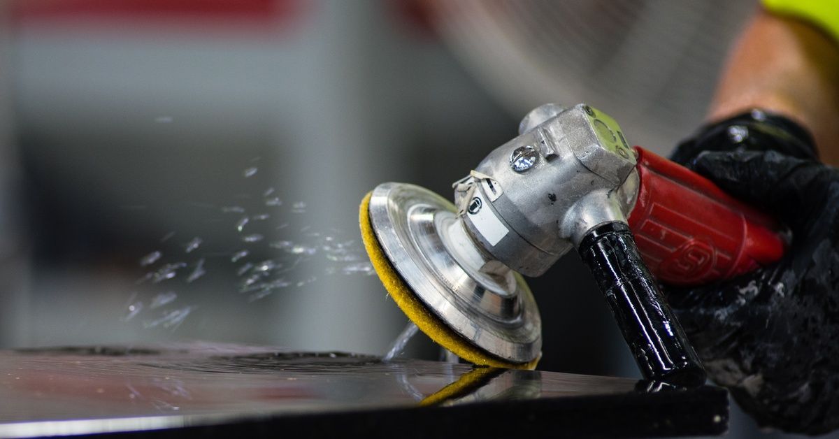 An employee wearing black gloves while polishing the edge of a granite countertop with a small handheld grinder.