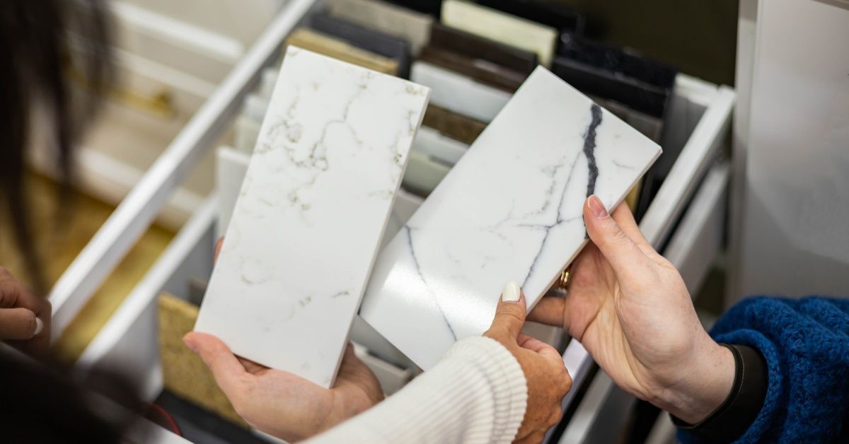 A person holding two rectangular marble countertop samples in their hands. Another person touches one of the samples.