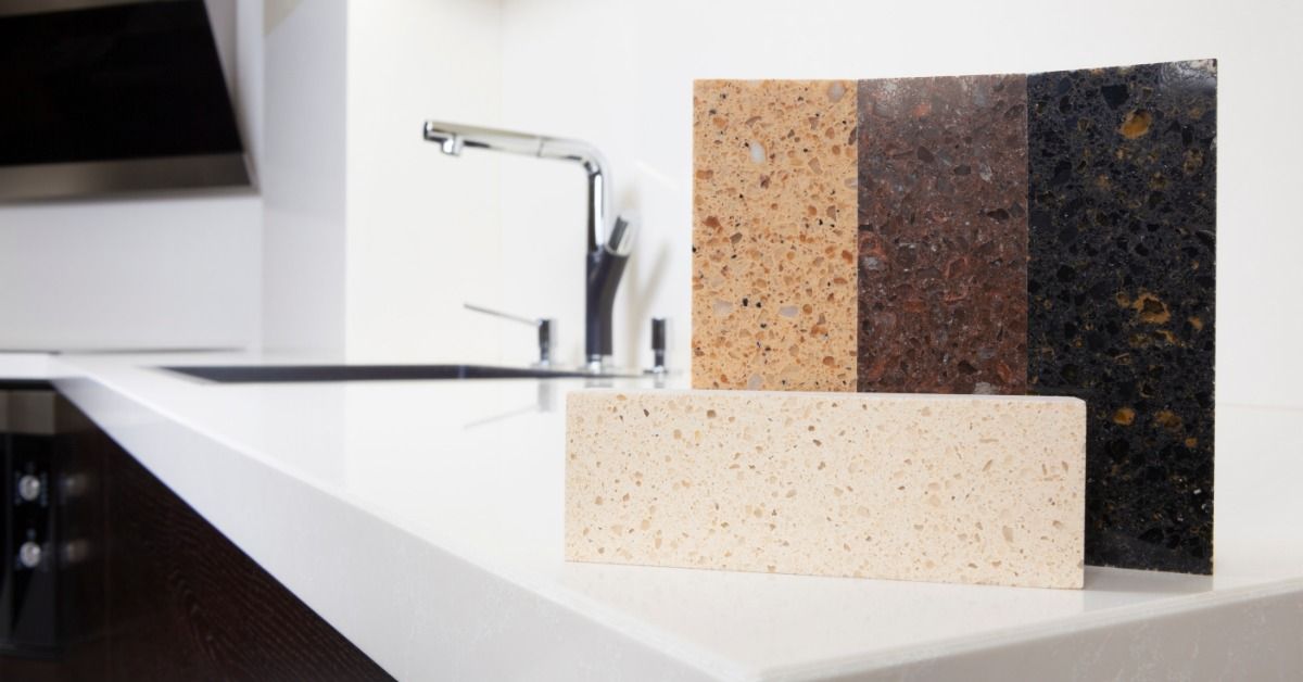 Four rectangular quartz samples on a countertop in a residential kitchen. A shiny sink is installed on the countertop.