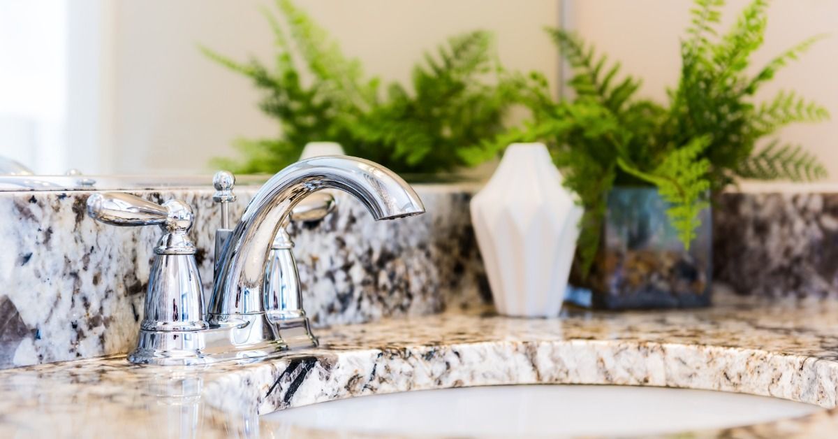 A bathroom sink on a granite countertop. The counter surface also has a plant in a white container.