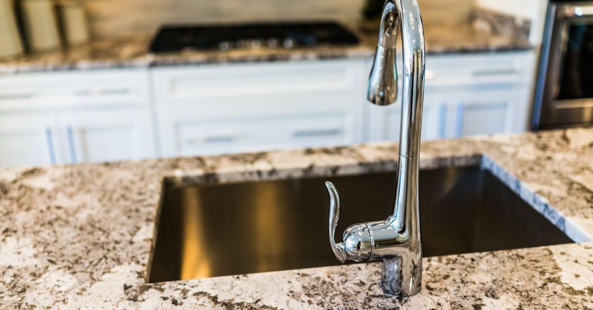 A granite kitchen countertop with a silver sink. White drawers with silver handles are installed under a nearby counter.