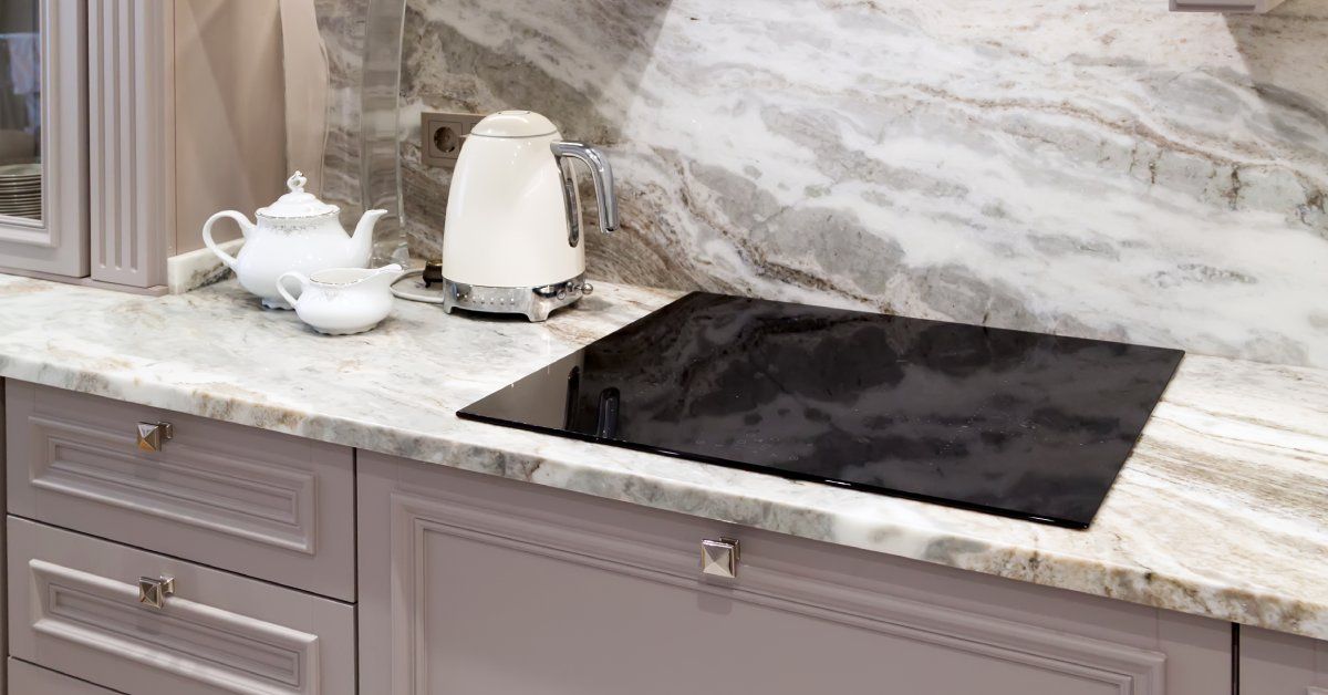 A black electric cooktop built into the quartz countertops with a white electric kettle and two-sized tea kettles.