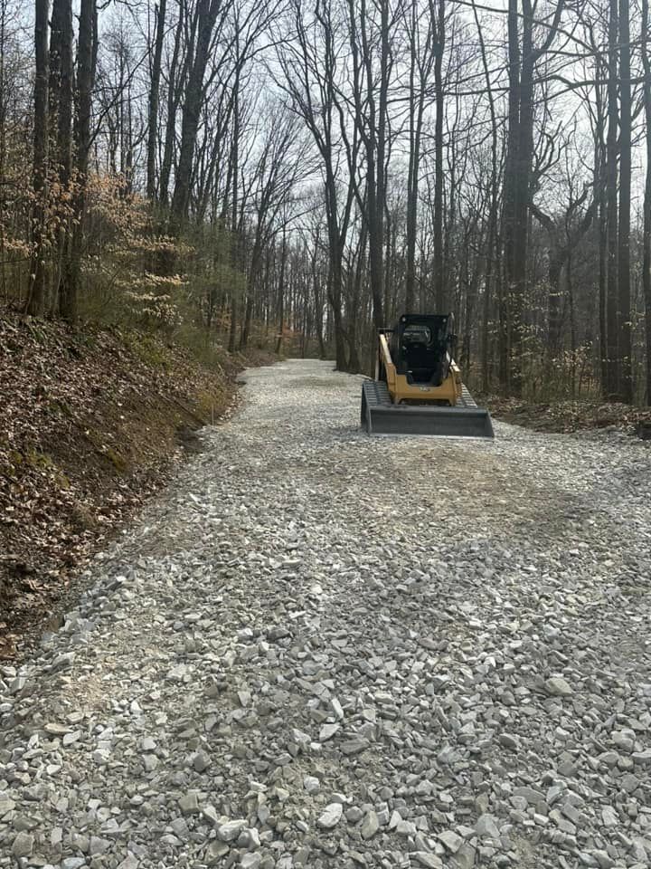 A bulldozer is driving down a gravel road in the woods.