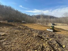 A tractor is plowing a dirt field with trees in the background.