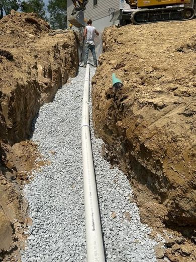 A man is standing in a trench next to a pipe.