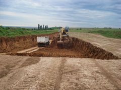A yellow excavator is digging a hole in a dirt field.