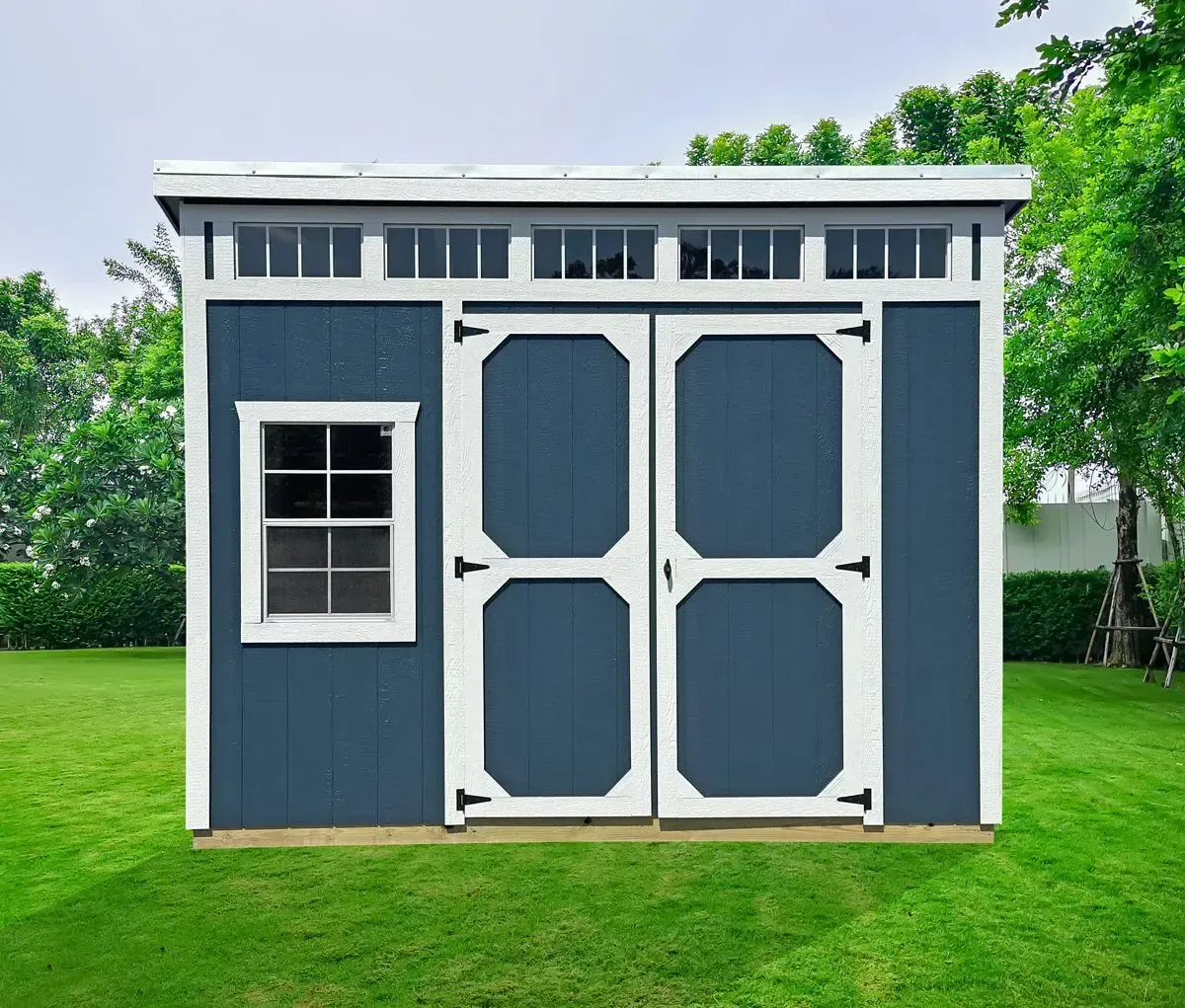 Blue shed with white trim, double doors, small window, in a green yard.