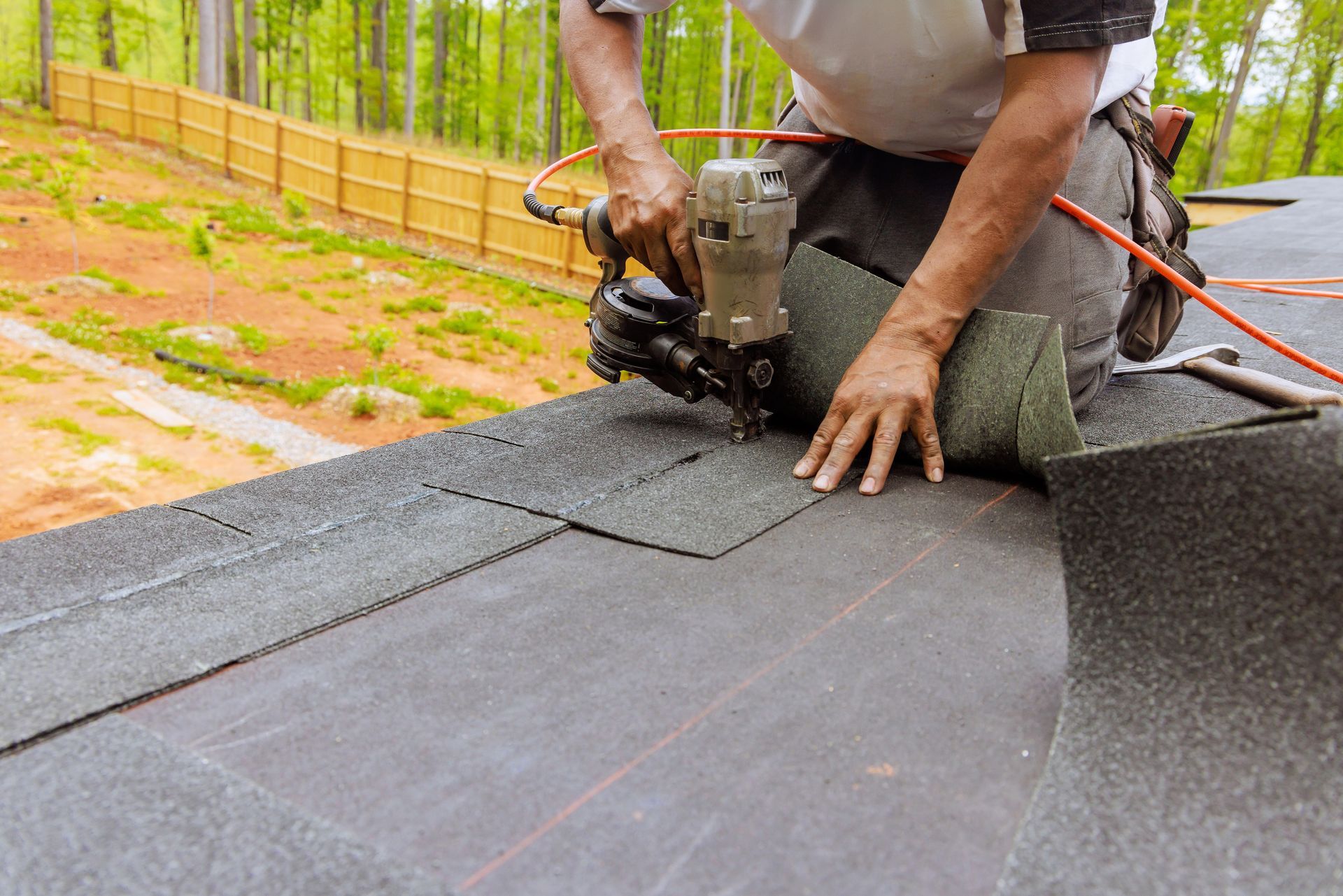 Worker using a nail gun to install roofing felt on a rooftop
