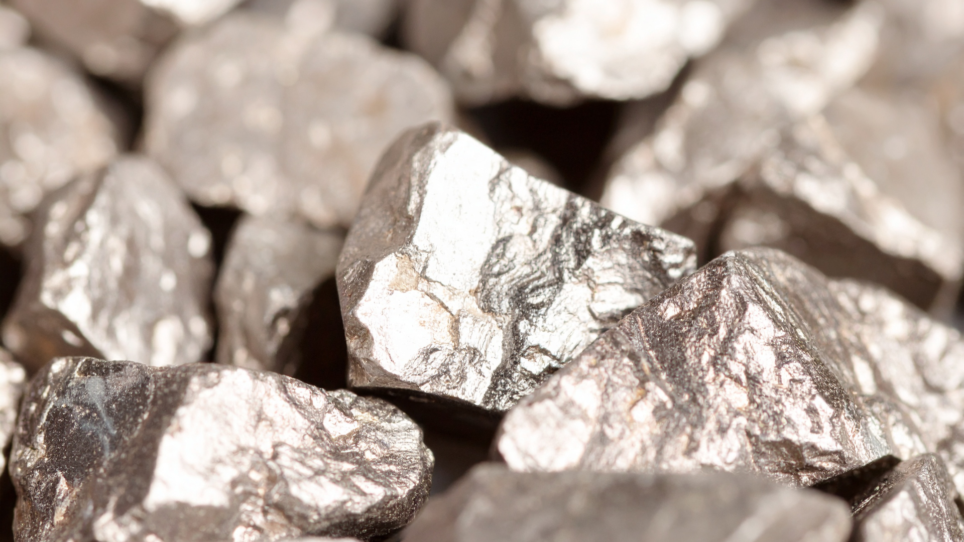 A close-up view of numerous irregular, metallic, silver-colored chunks of raw ore.
