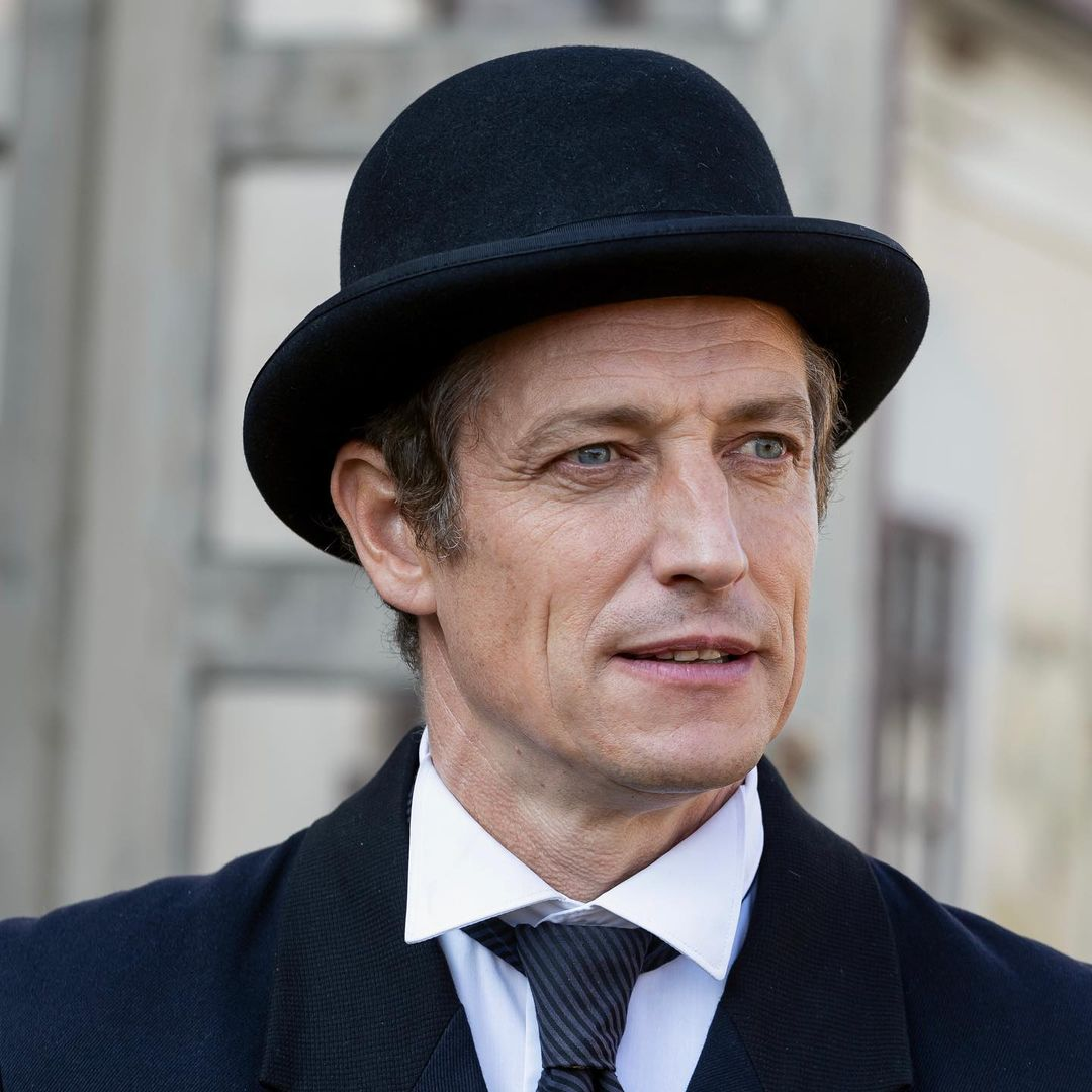 Man in bowler hat and suit, looking to the side with a neutral expression.