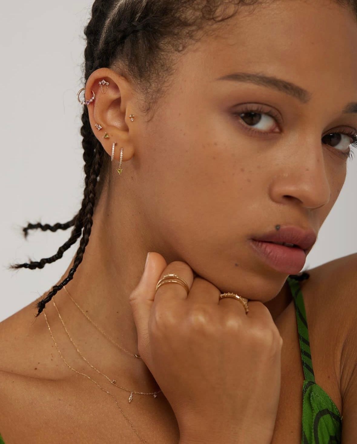 Woman with multiple ear piercings and gold rings. She looks directly at the camera with a neutral expression.
