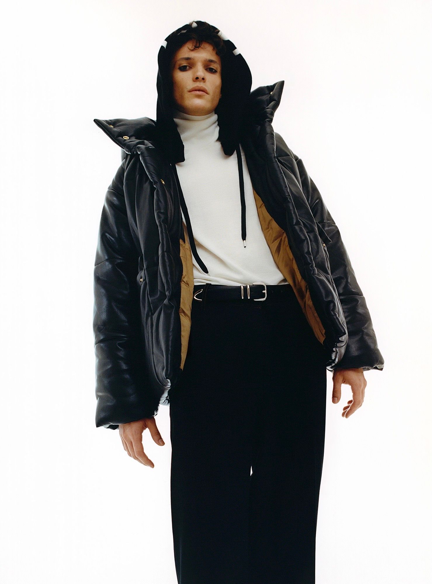 Person wearing a black puffer jacket with a hood, white turtleneck, black skirt, and belt.