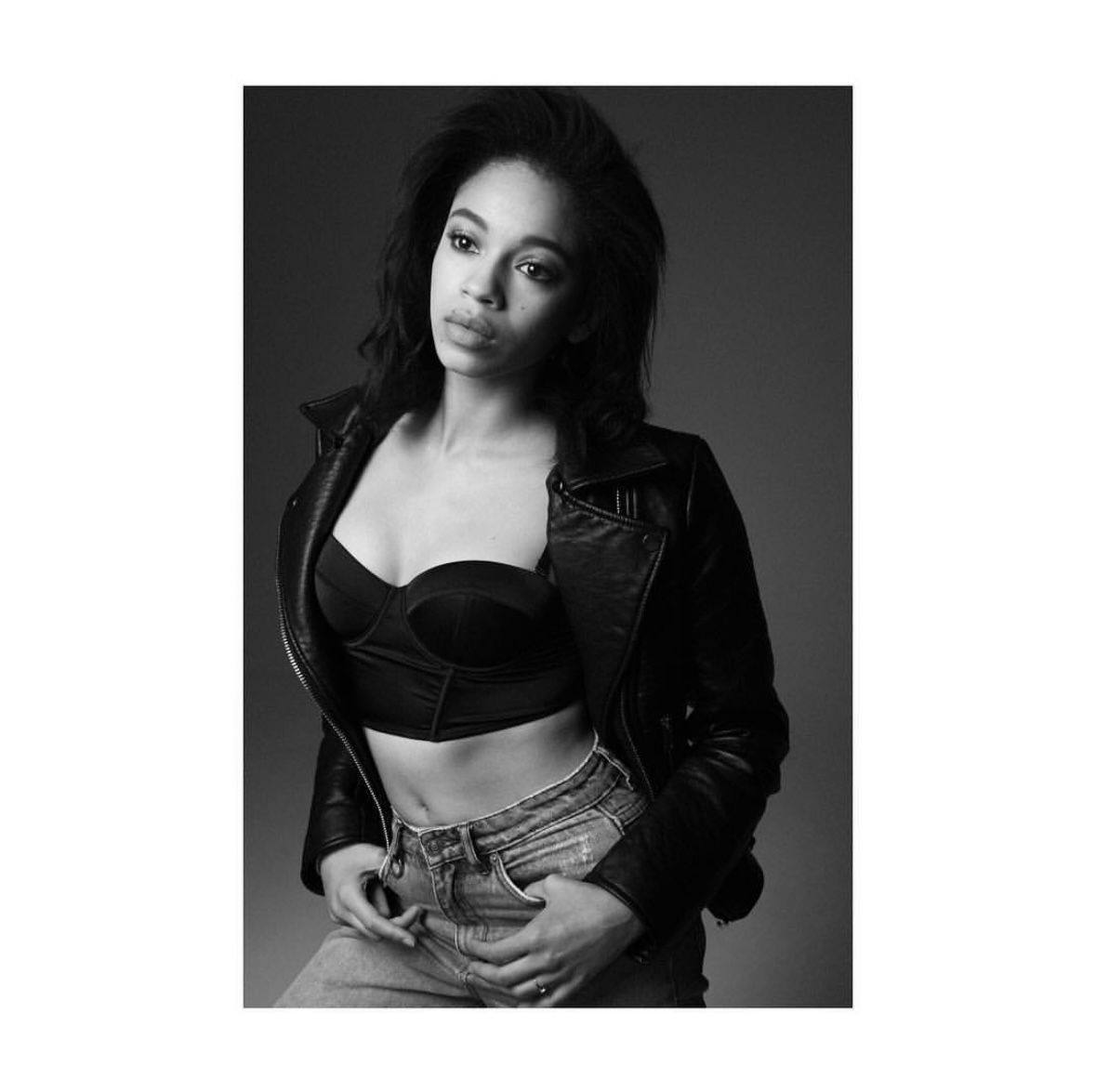 Woman in a leather jacket and bra poses with hands in front of waist.