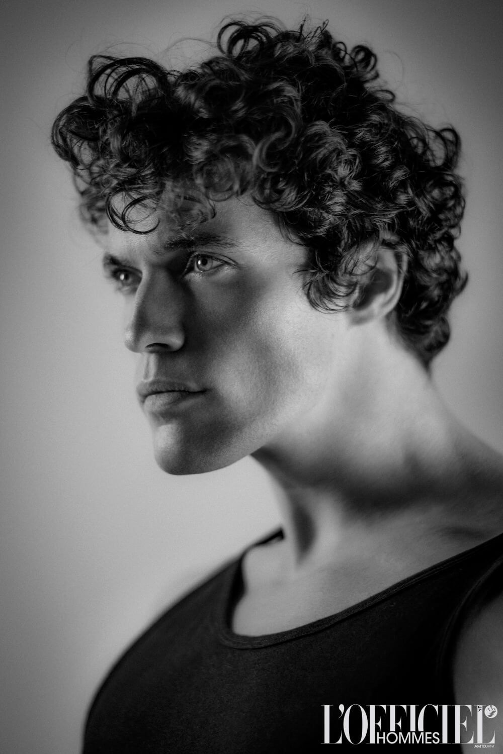Man with curly hair in a black tank top, looking to the side with a serious expression.