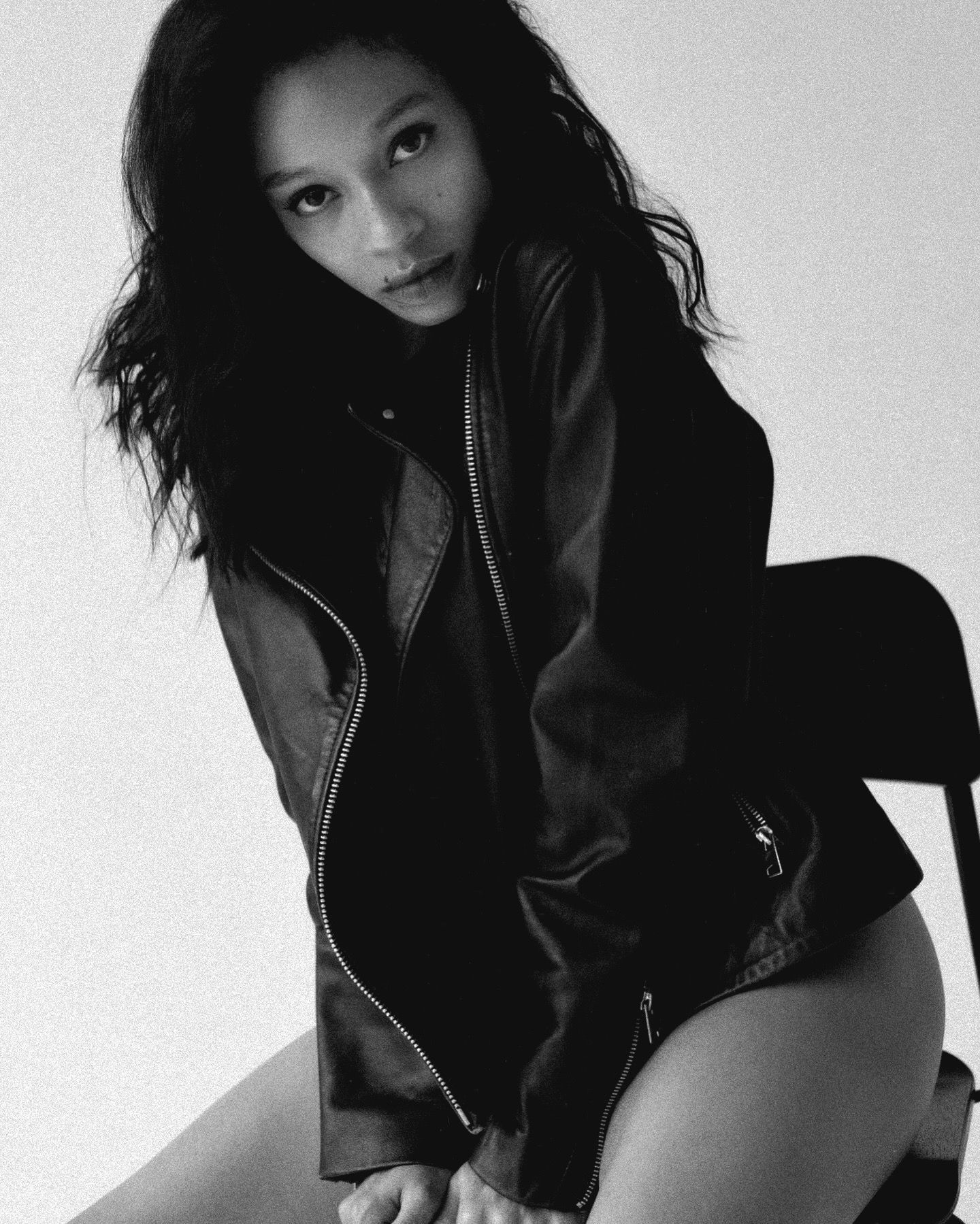 Woman in a leather jacket, seated, looking at the camera. Black and white.
