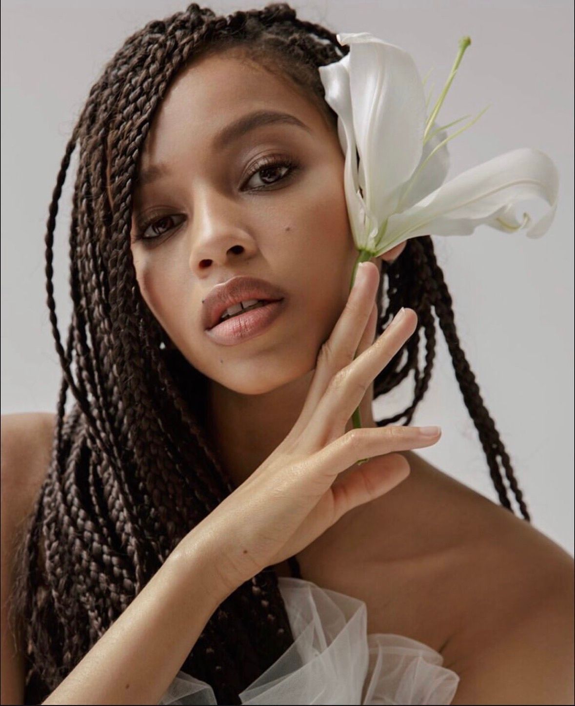 Woman with braided hair, a white flower near her face, looking at the camera.