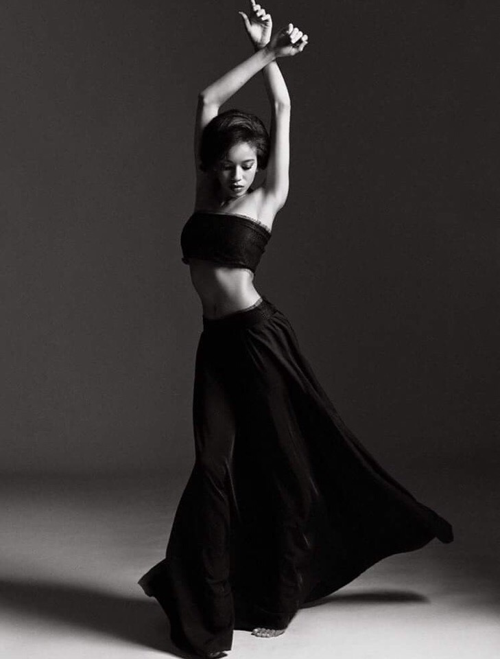 Woman in black strapless top and flowing skirt, arms raised, dancing.