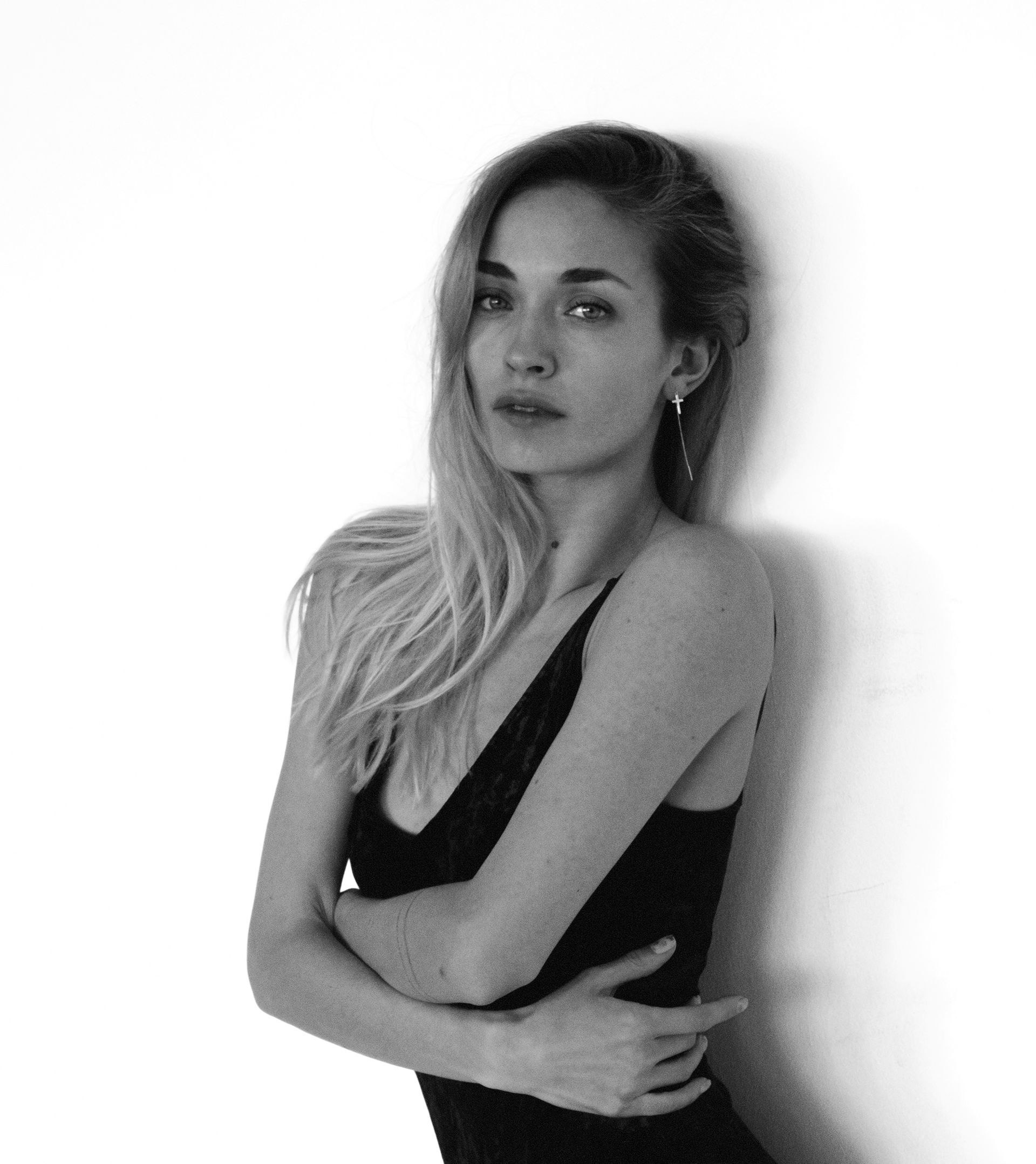 Woman leaning against a white wall, arms crossed, wearing a black top. Black and white photo.