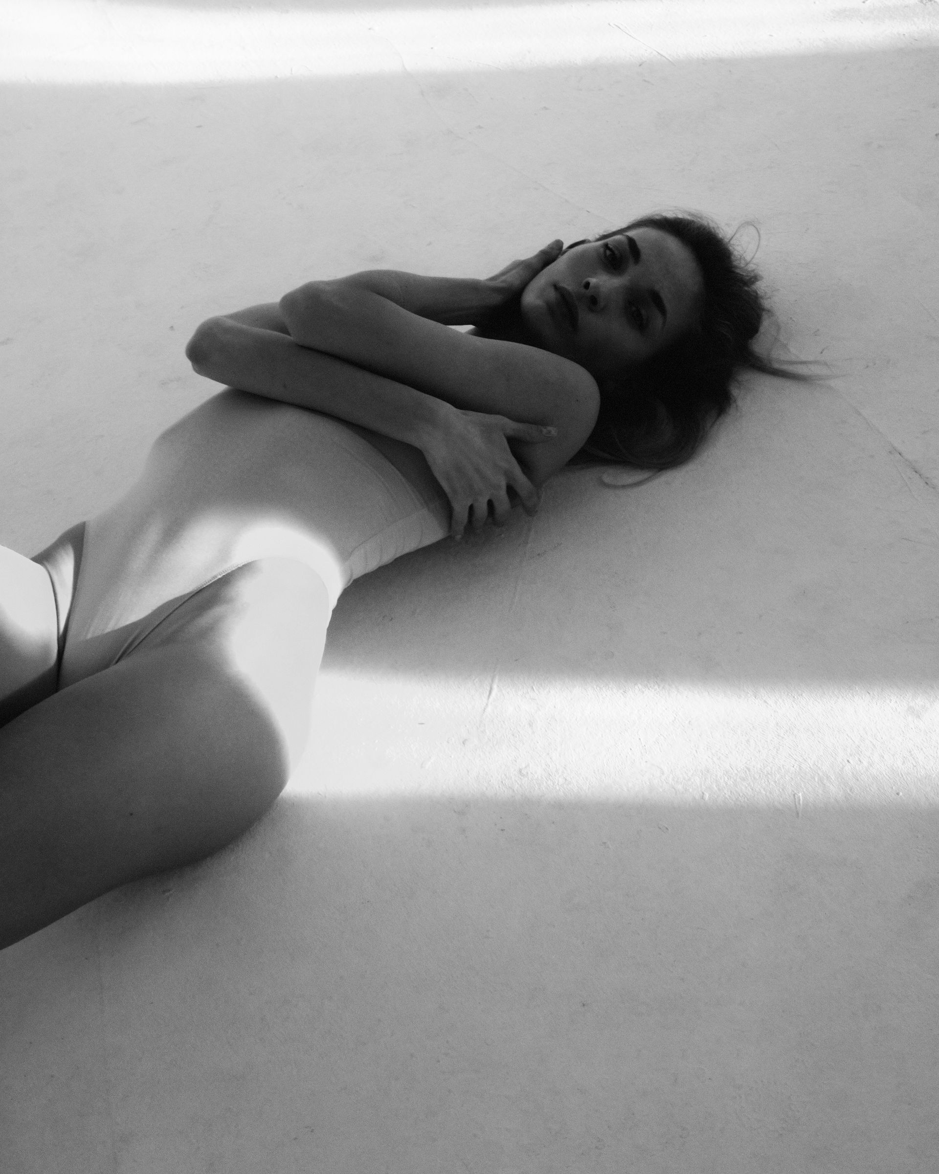 Woman lying down, arms crossed, in a brightly lit space. Black and white photo.