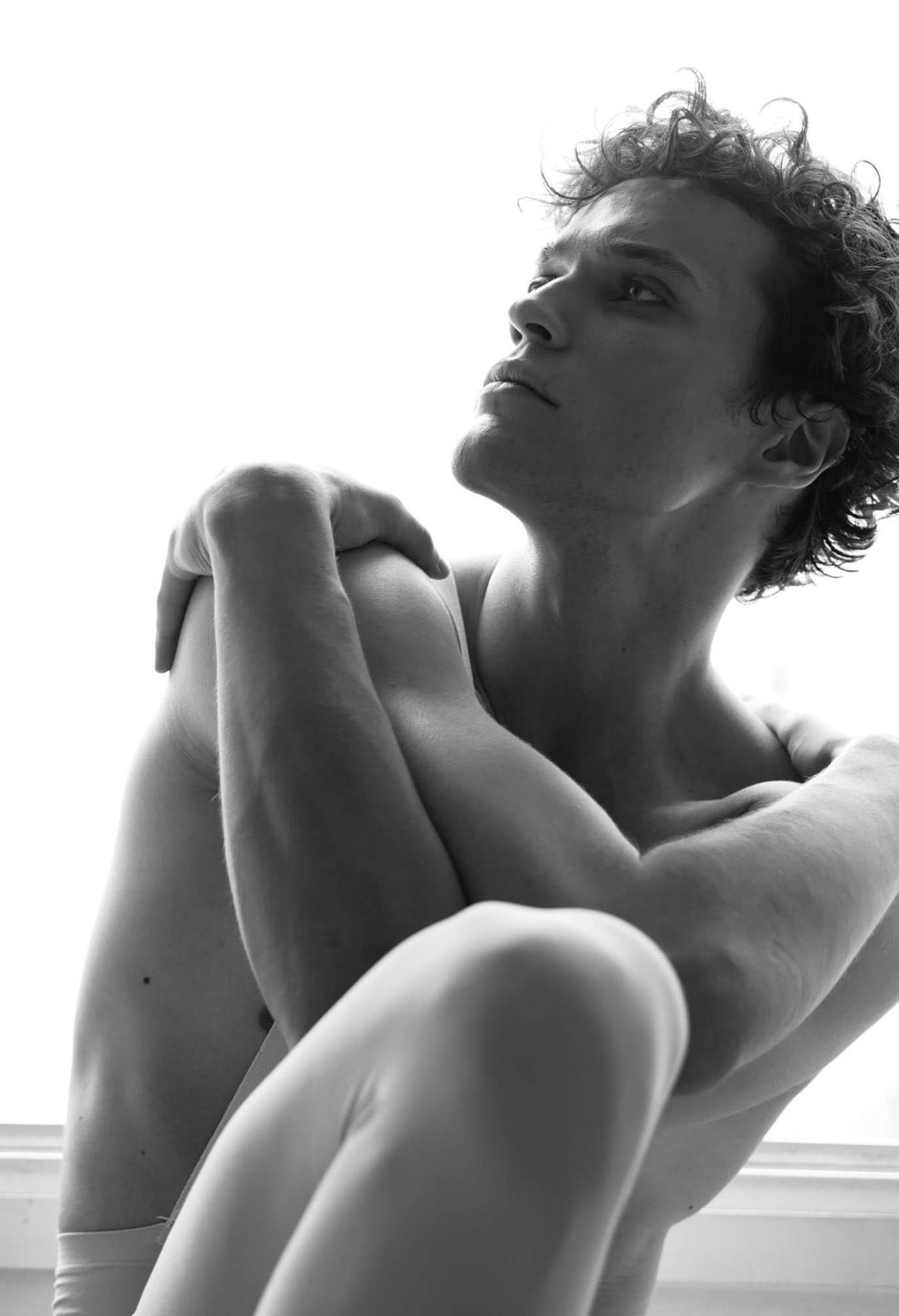 Man with curly hair, arms crossed, looking upward in a monochrome photo.