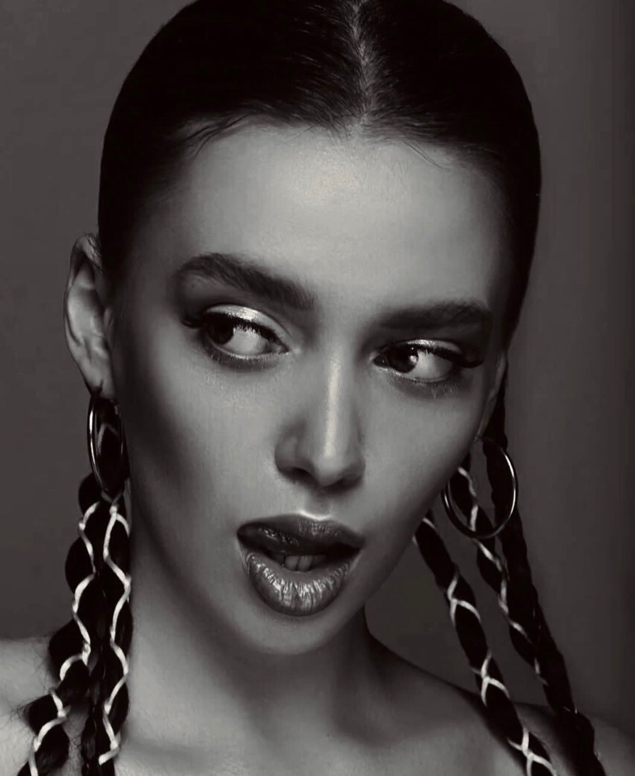 Woman with braids, dramatic eye makeup, and open mouth, looking off to the side. Black and white.