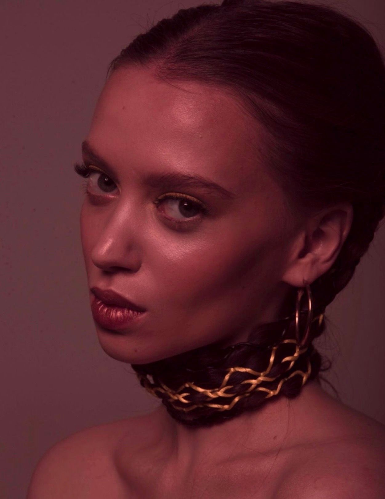 Woman with golden choker and hoop earrings, looking at the camera.