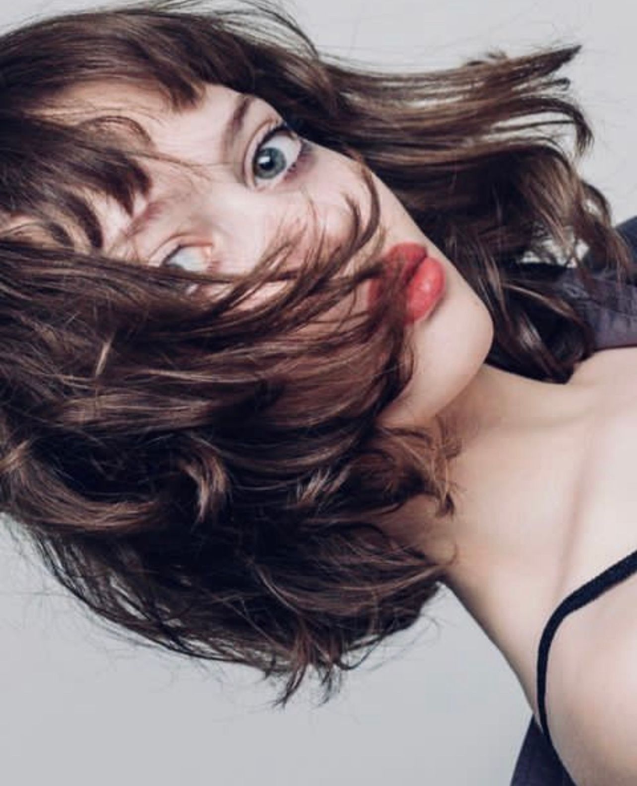 Woman with brown wavy hair and red lipstick, looking up, hair partially covering face.